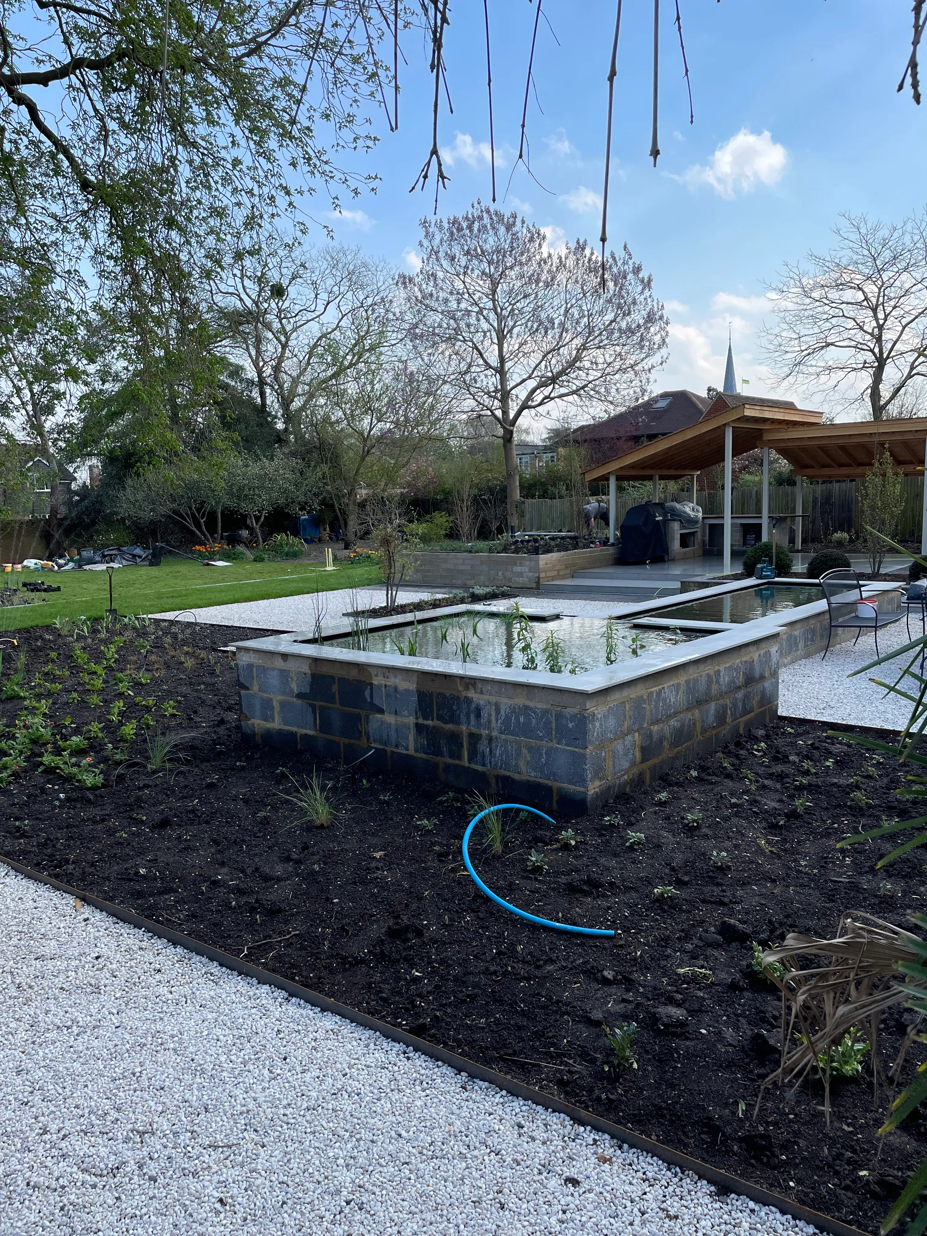 View across koi pond towards outdoor kitchen and dining terrace in Sawbridgeworth