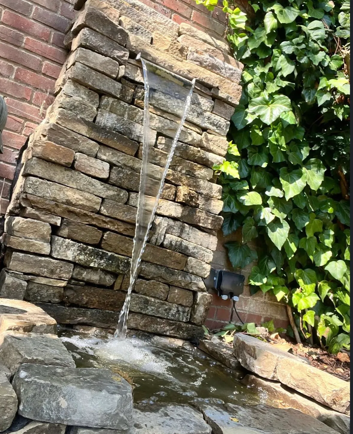 Natural stone water feature pouring into koi pond in Sawbridgeworth garden